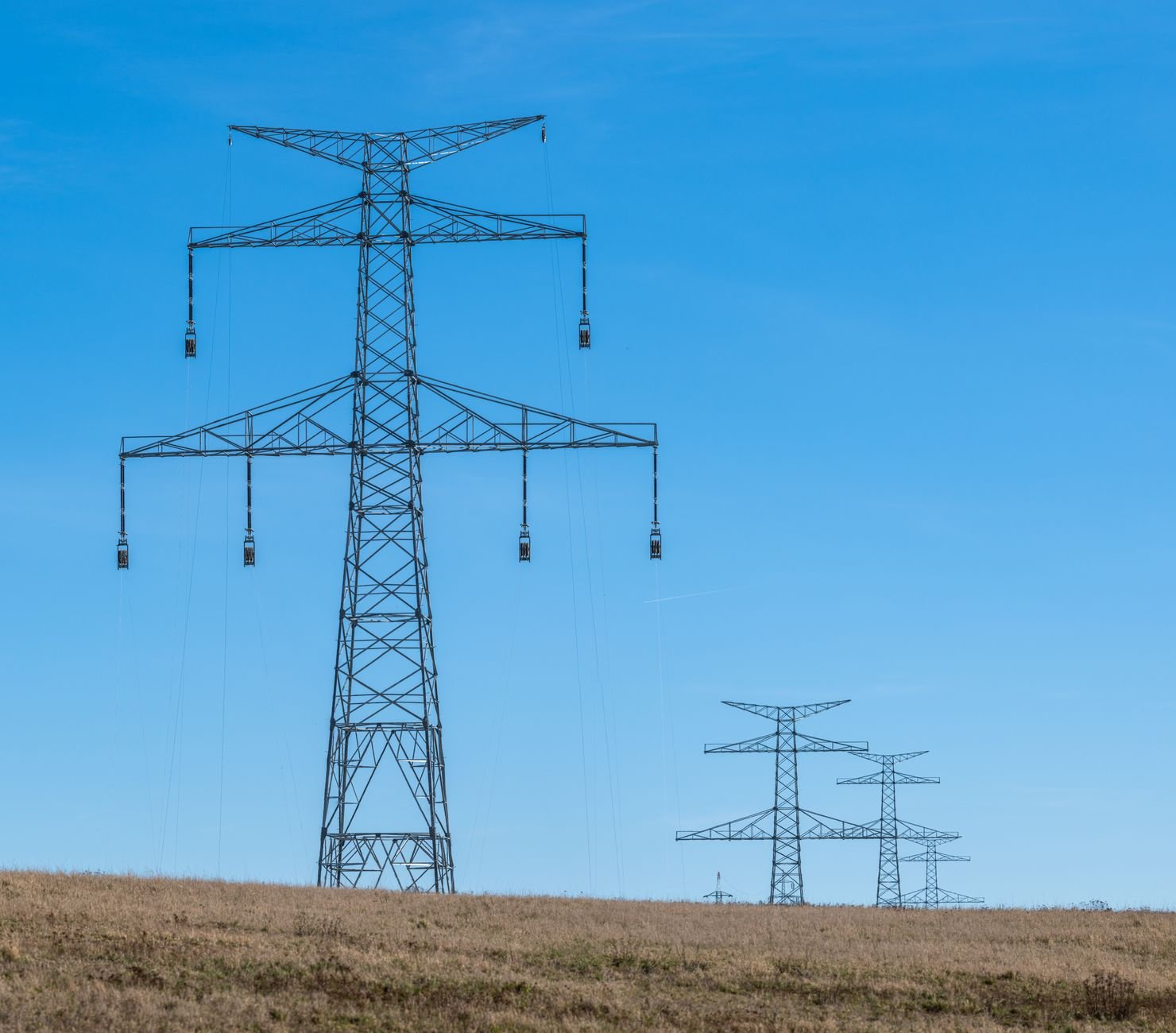 High-voltage transmission towers and power lines running through open countryside