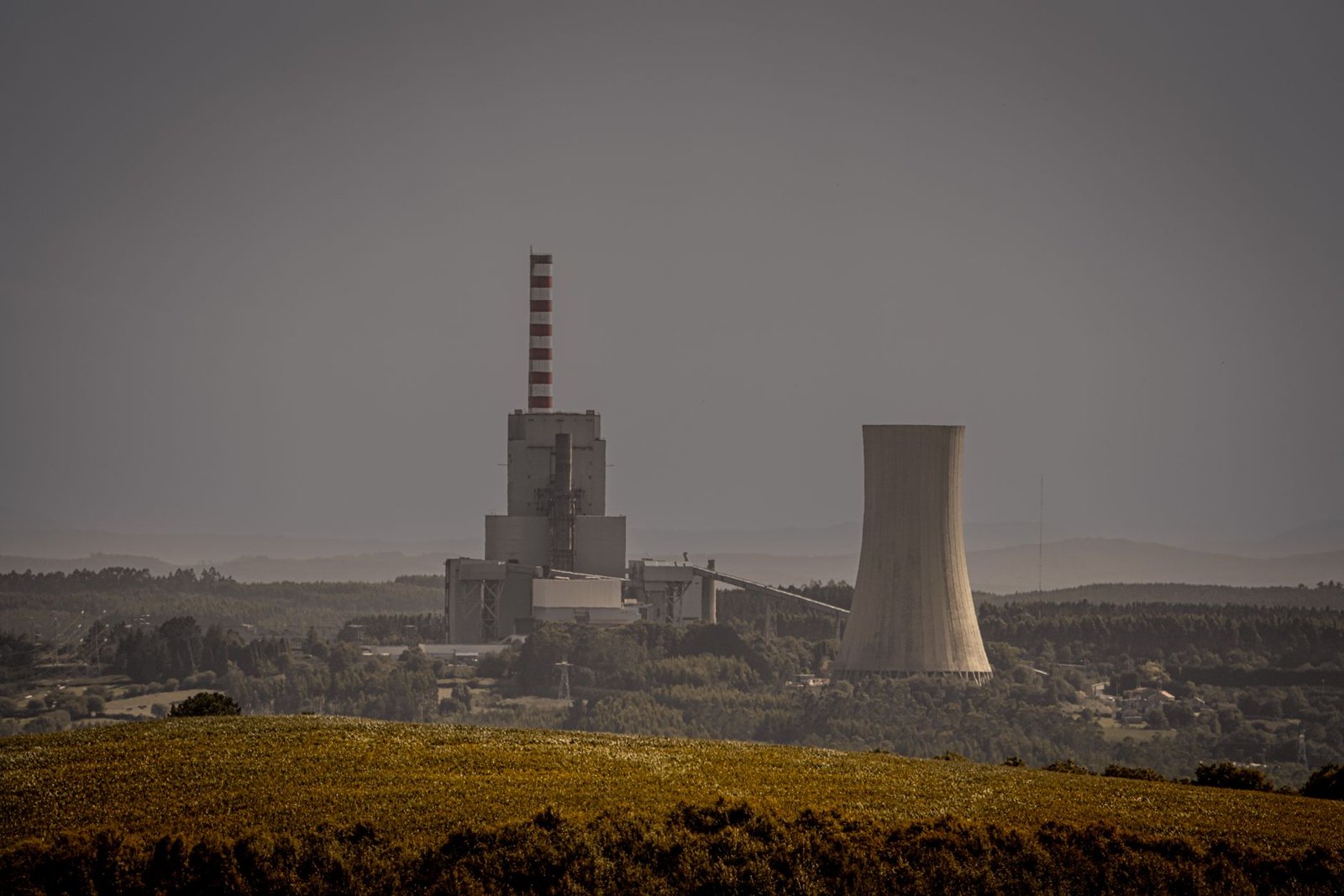 A natural gas combined-cycle power plant with cooling stacks against an overcast sky