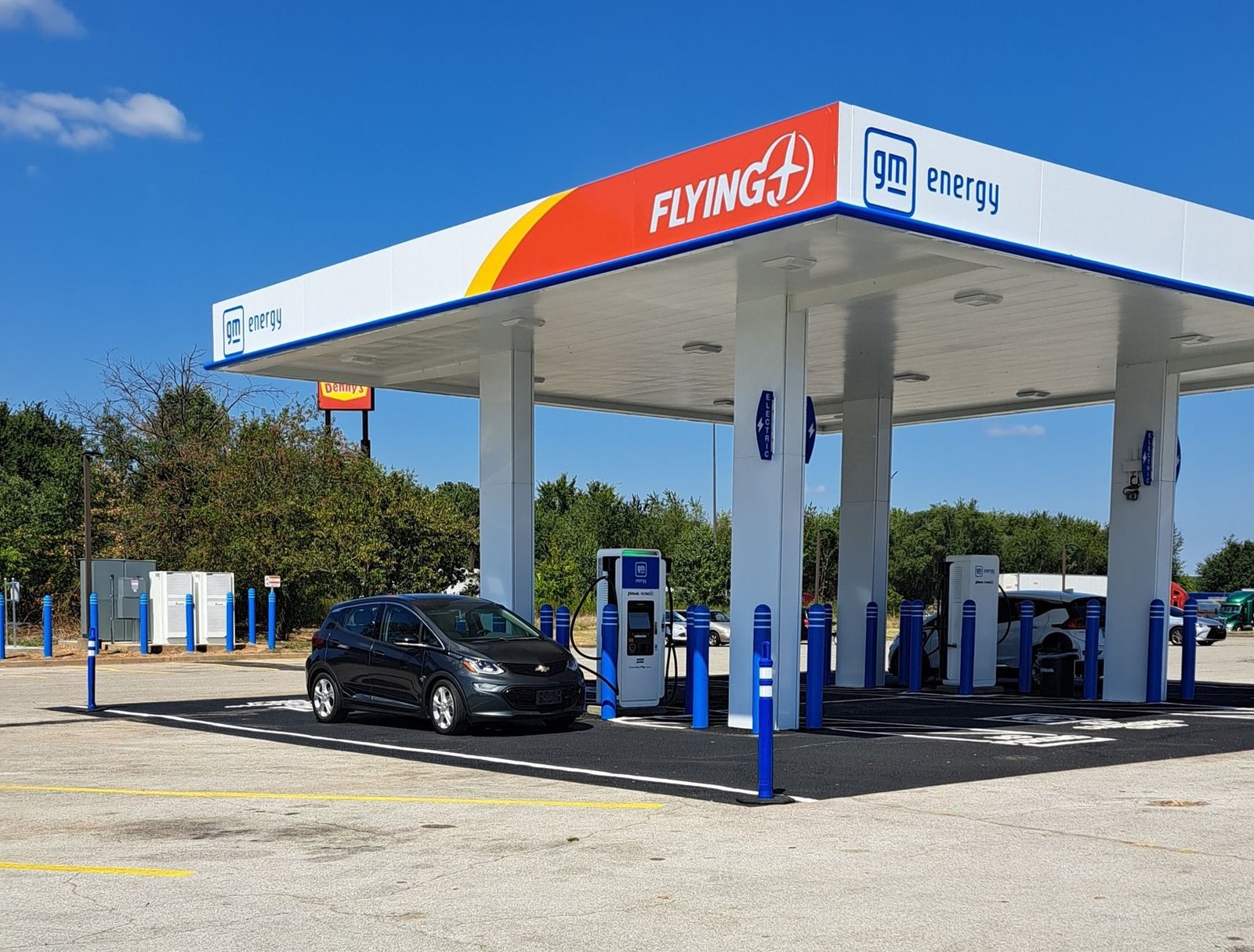 Electric cars plugged into a row of fast chargers at a busy highway service area