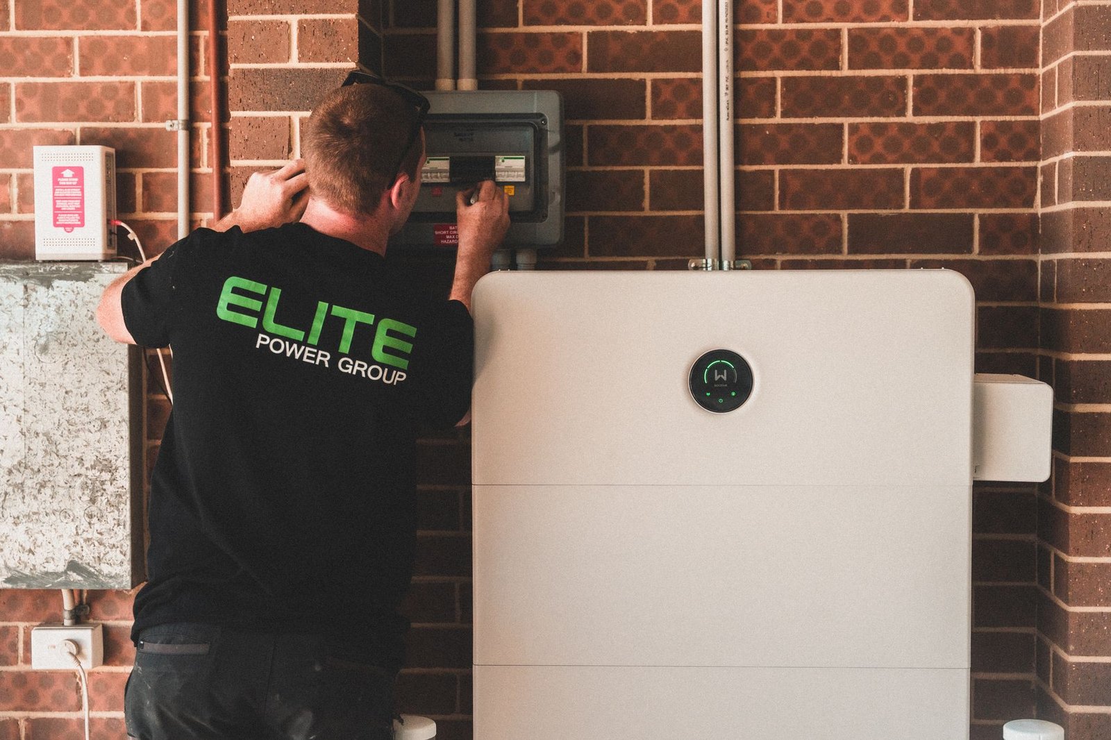 A home battery unit mounted on a residential garage wall beside an electrical panel