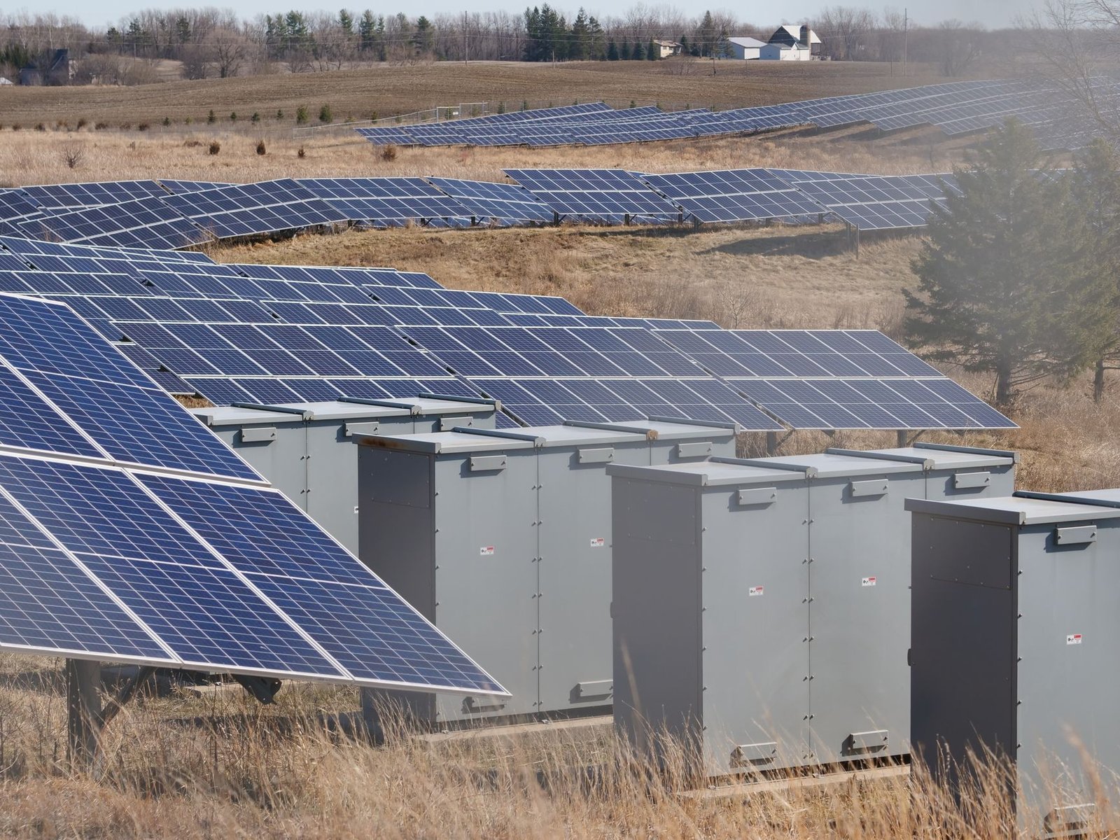 Grid-scale battery storage containers lined up beside a large solar array